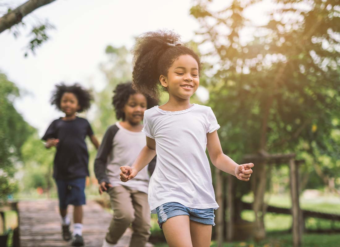 Child Life Insurance - Cute Young Girl Focus Playing Outdoors and Running Ahead of Her Two Older Siblings in the Summertime at Sunset